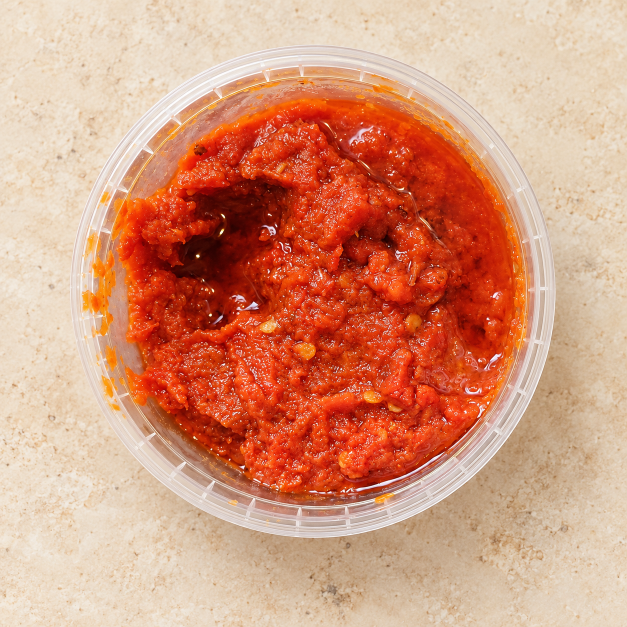 A close view of Trisha’s red pepper sauce in its open clear tub on a clean background